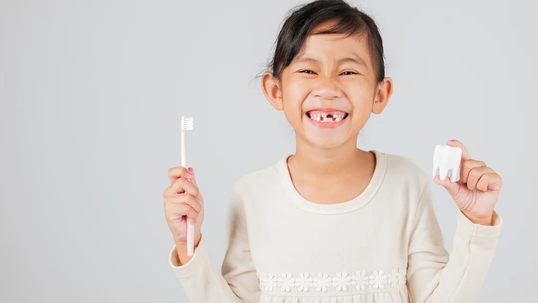 A young patient smiling at Brooklyn Dental Group, holding a toothbrush and a model tooth